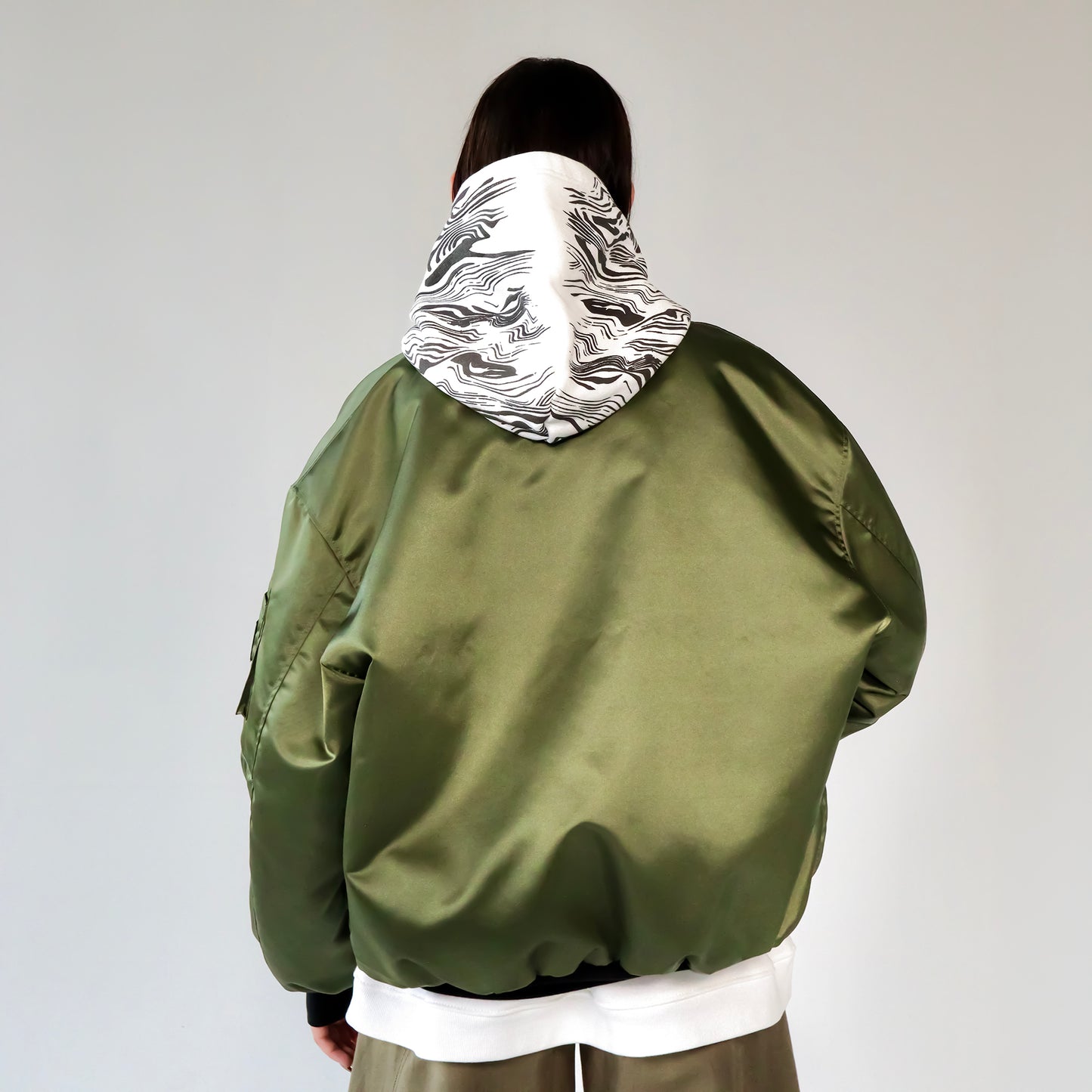 Person wearing a green bomber jacket with white printed hoodie underneath on a white background