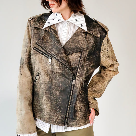 Person wearing a patterned black and brown soft lambskin leather aviator style jacket over a white shirt with black embroidered ant designs on a light gray background. made by mucina studio in latvia