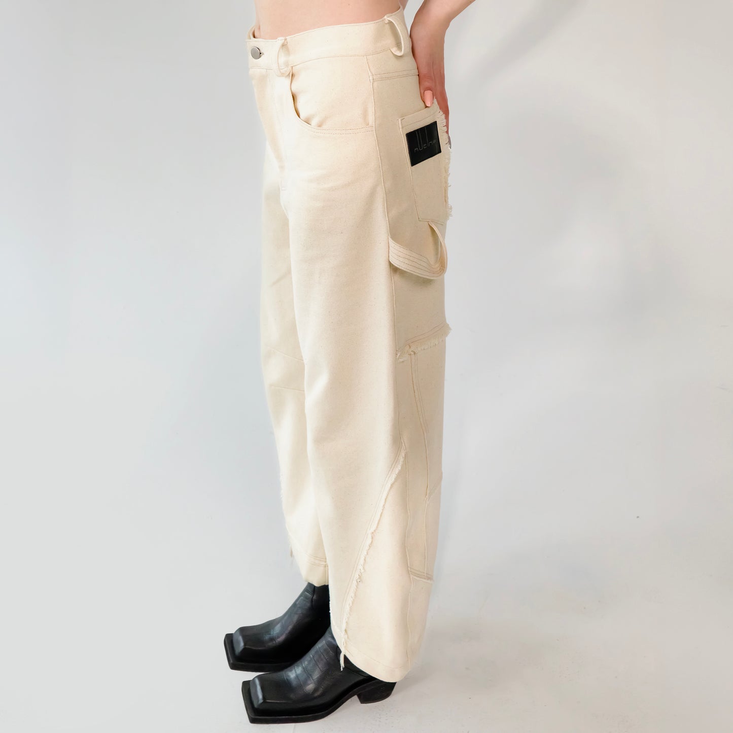 Beige barrel-leg cargo pants with patch detailing worn with a beige bomber jacket on a white background