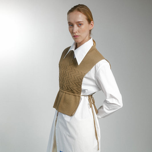Woman wearing a brown patterned vest over a white shirt on a gray background