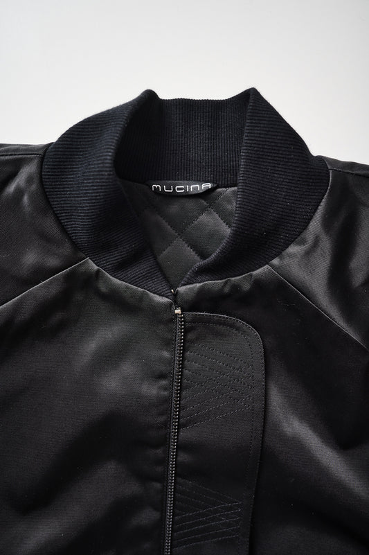 Close-up of a black bomber jacket with a visible brand tag, showing the collar and part of the sleeve.
