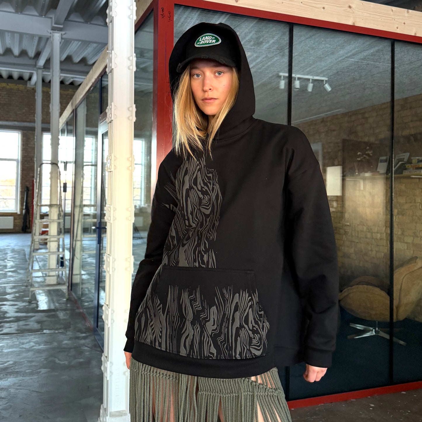 Person wearing a black hoodie with a unique tree printed design on the chest, standing in an indoor setting.