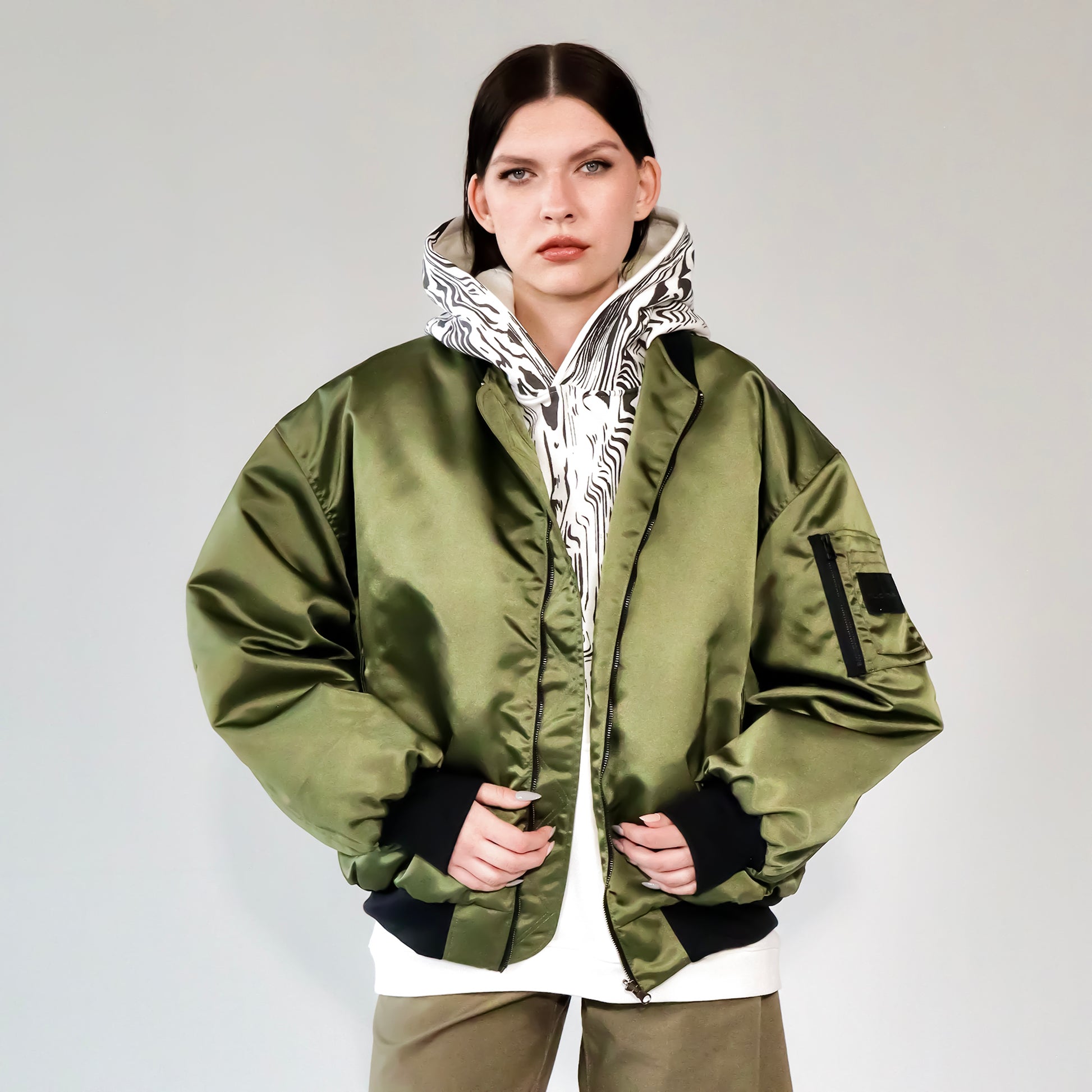 Person wearing a green bomber jacket with white printed hoodie underneath on a white backgorund