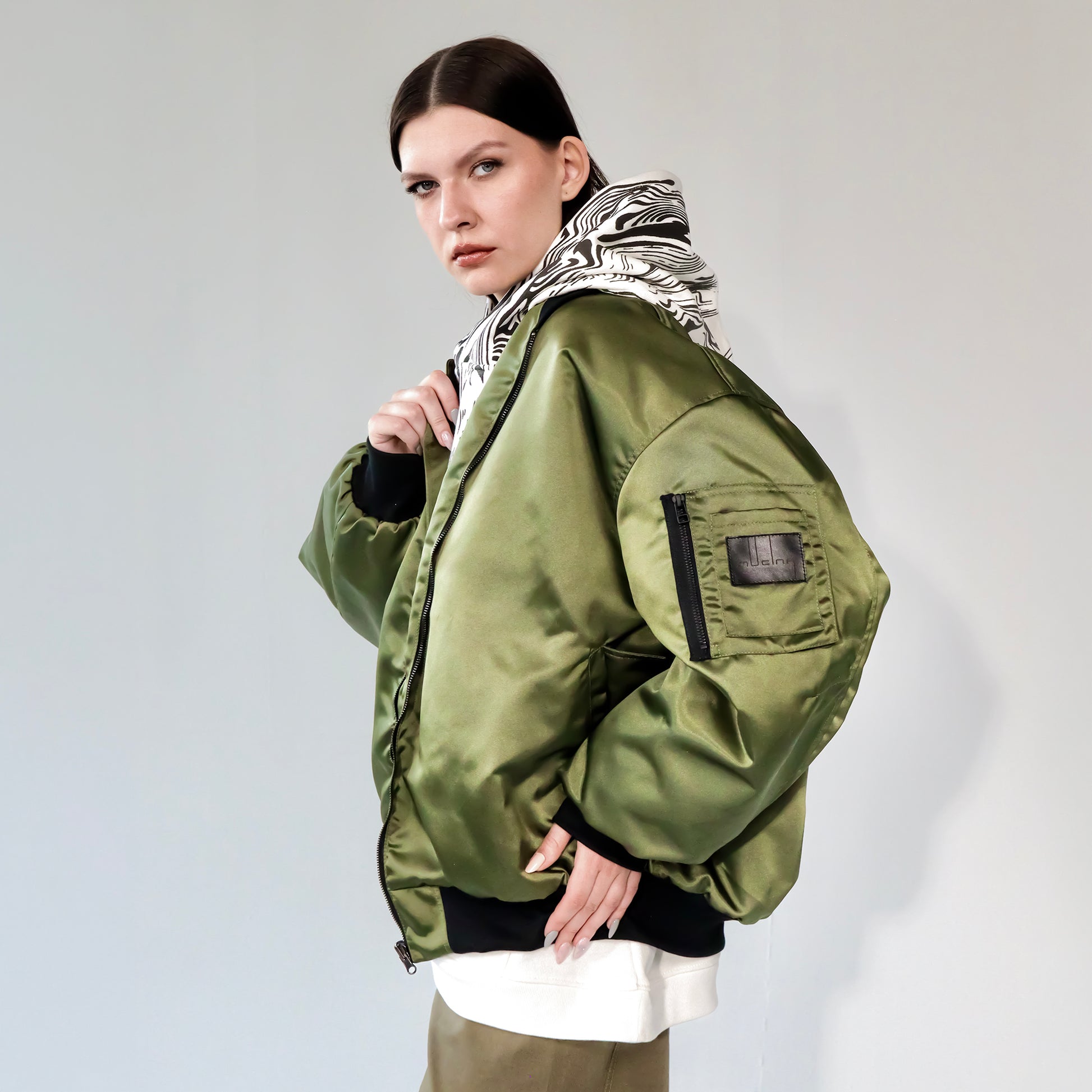 Person wearing a green bomber jacket with white printed hoodie underneath on a white background 