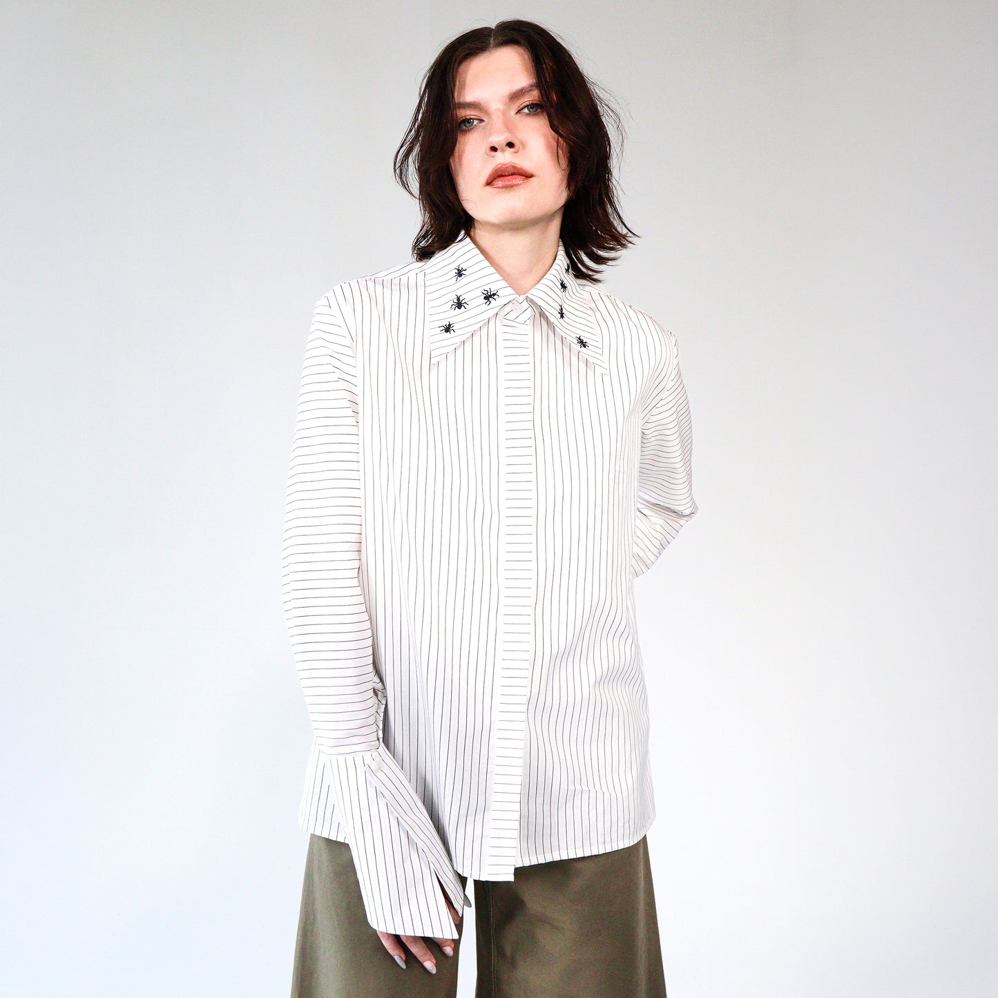 White stripped shirt with black ant hand embroidered designs on a plain background