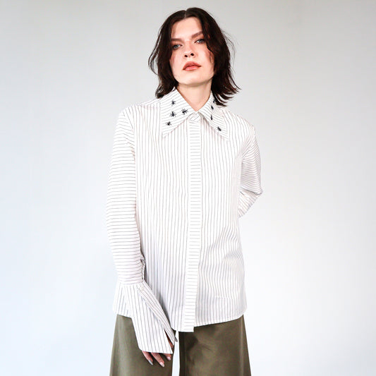 White stripped shirt with black ant hand embroidered designs on a plain background