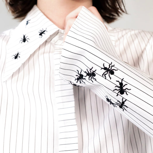 White stripped shirt with black ant hand embroidered designs on a plain background