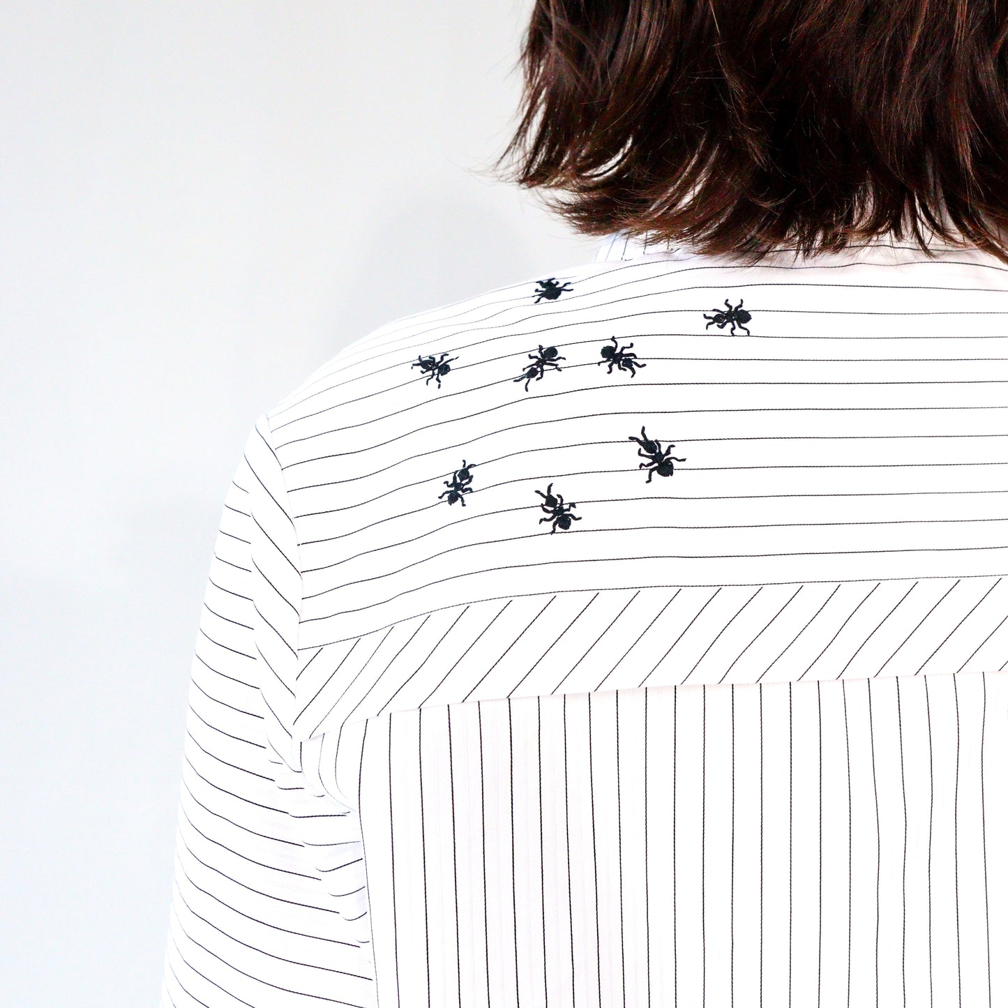 White stripped shirt with black ant hand embroidered designs on a plain background