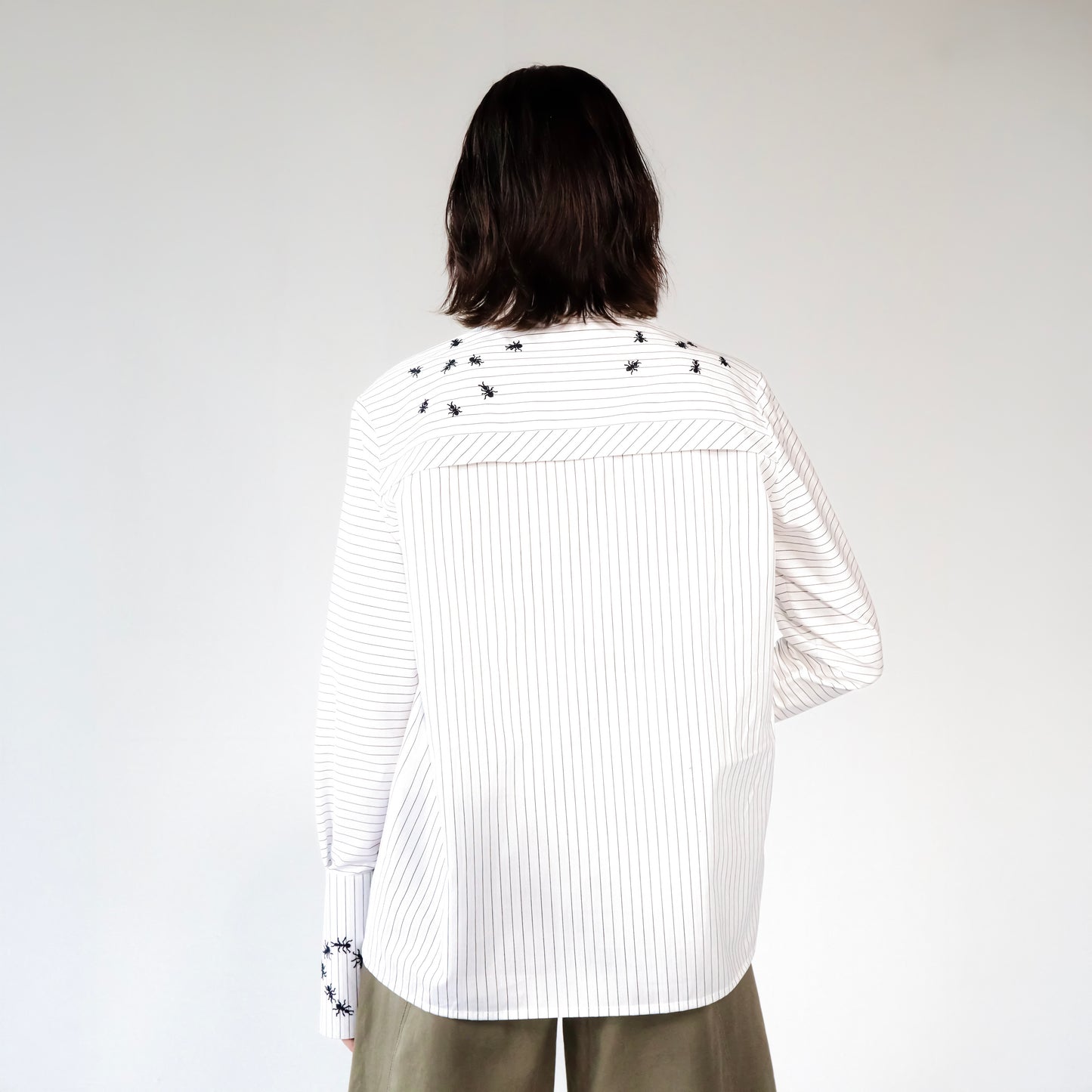 White stripped shirt with black ant hand embroidered designs on a plain background