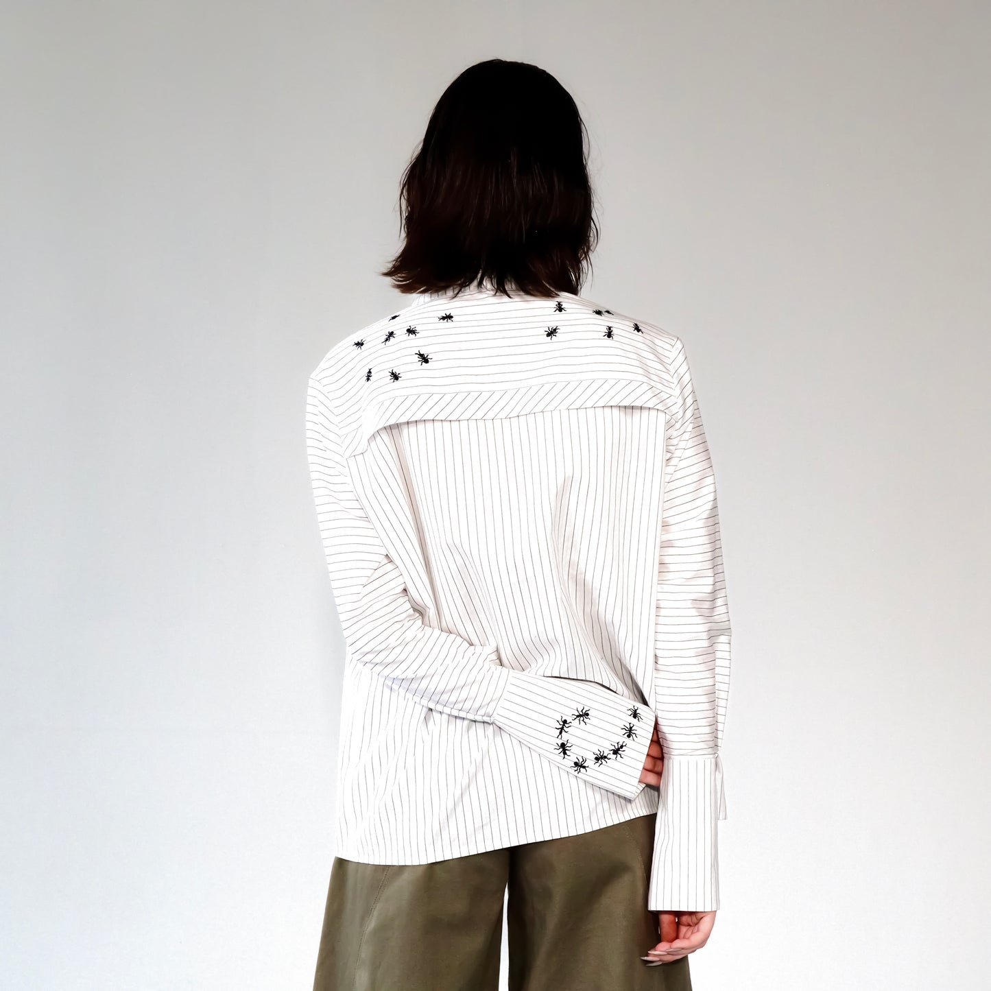White stripped shirt with black ant hand embroidered designs on a plain background