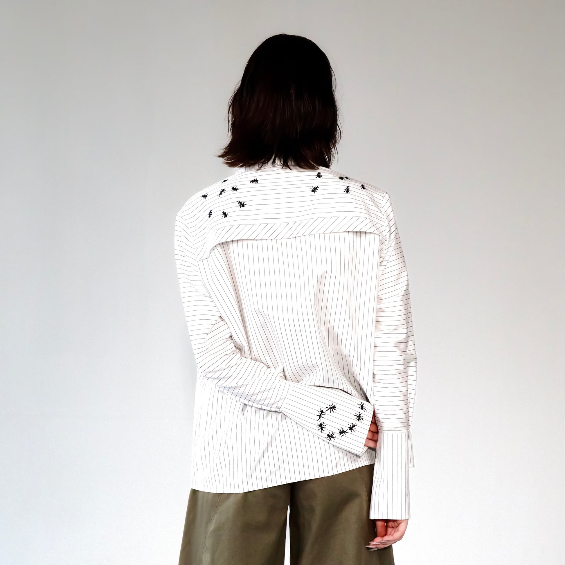 White stripped shirt with black ant hand embroidered designs on a plain background