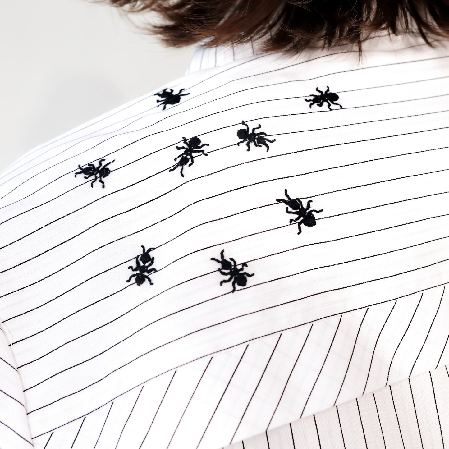 White stripped shirt with black ant hand embroidered designs on a plain background