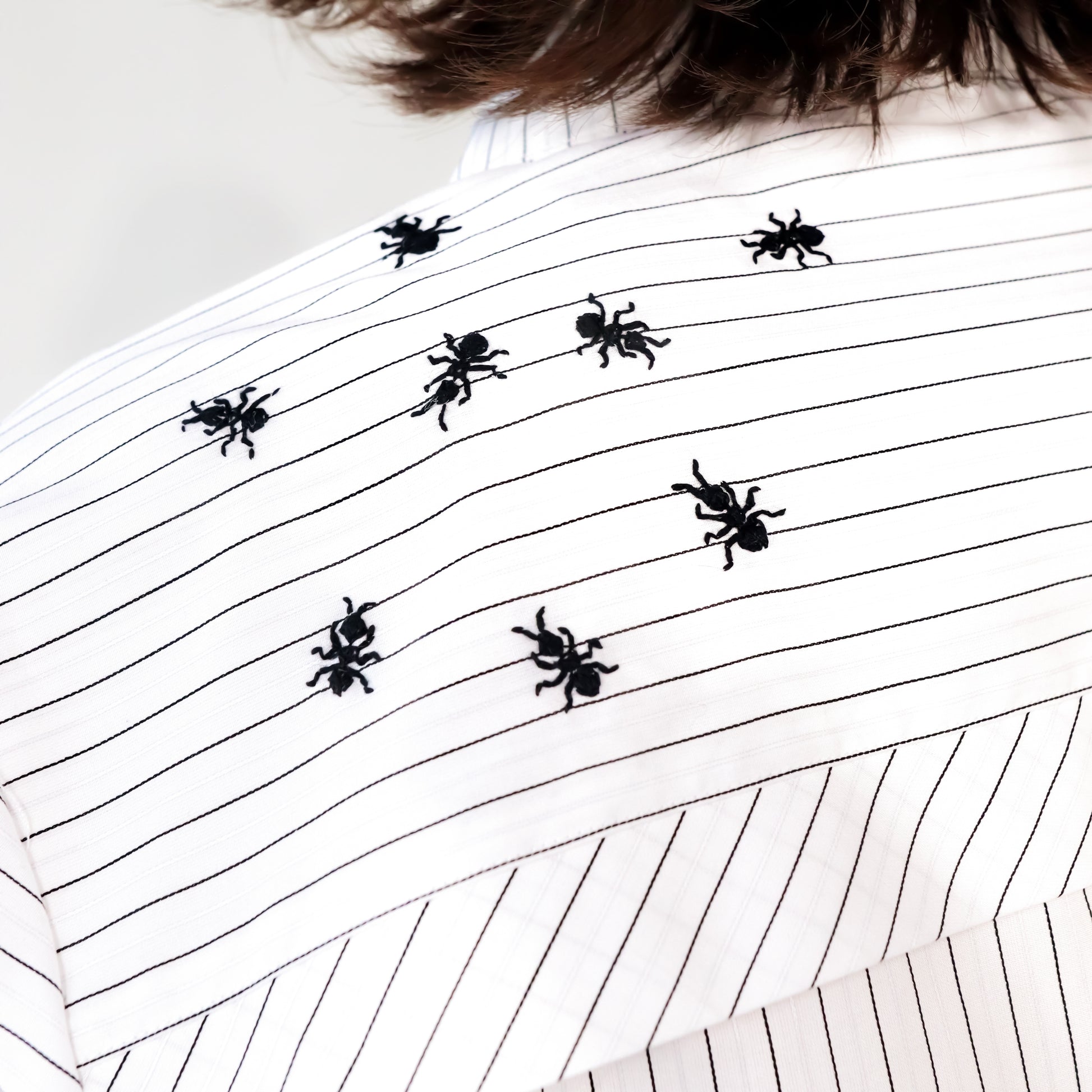 White stripped shirt with black ant hand embroidered designs on a plain background