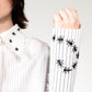 White stripped shirt with black ant hand embroidered designs on the cuff on a plain background