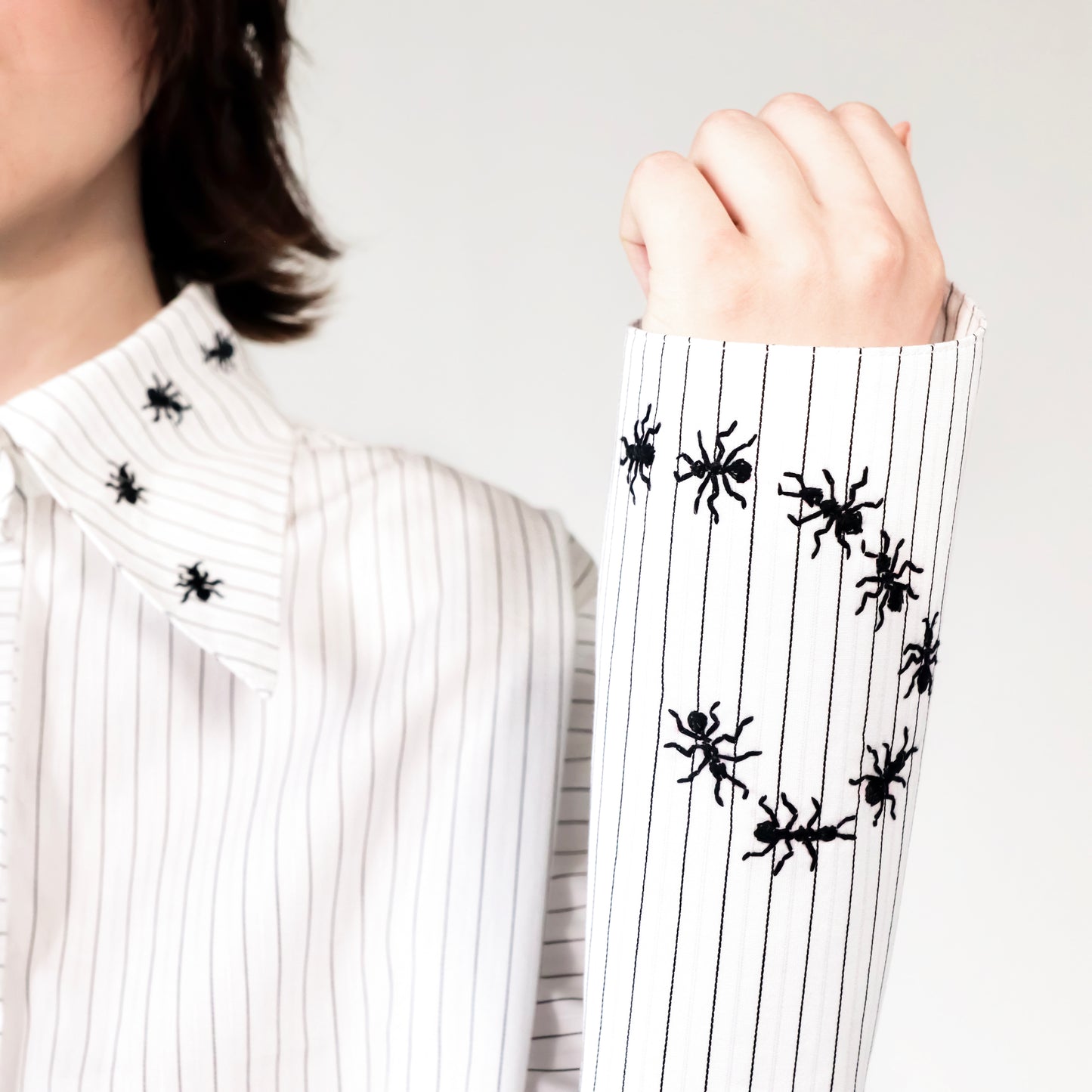 White stripped shirt with black ant hand embroidered designs on the cuff on a plain background