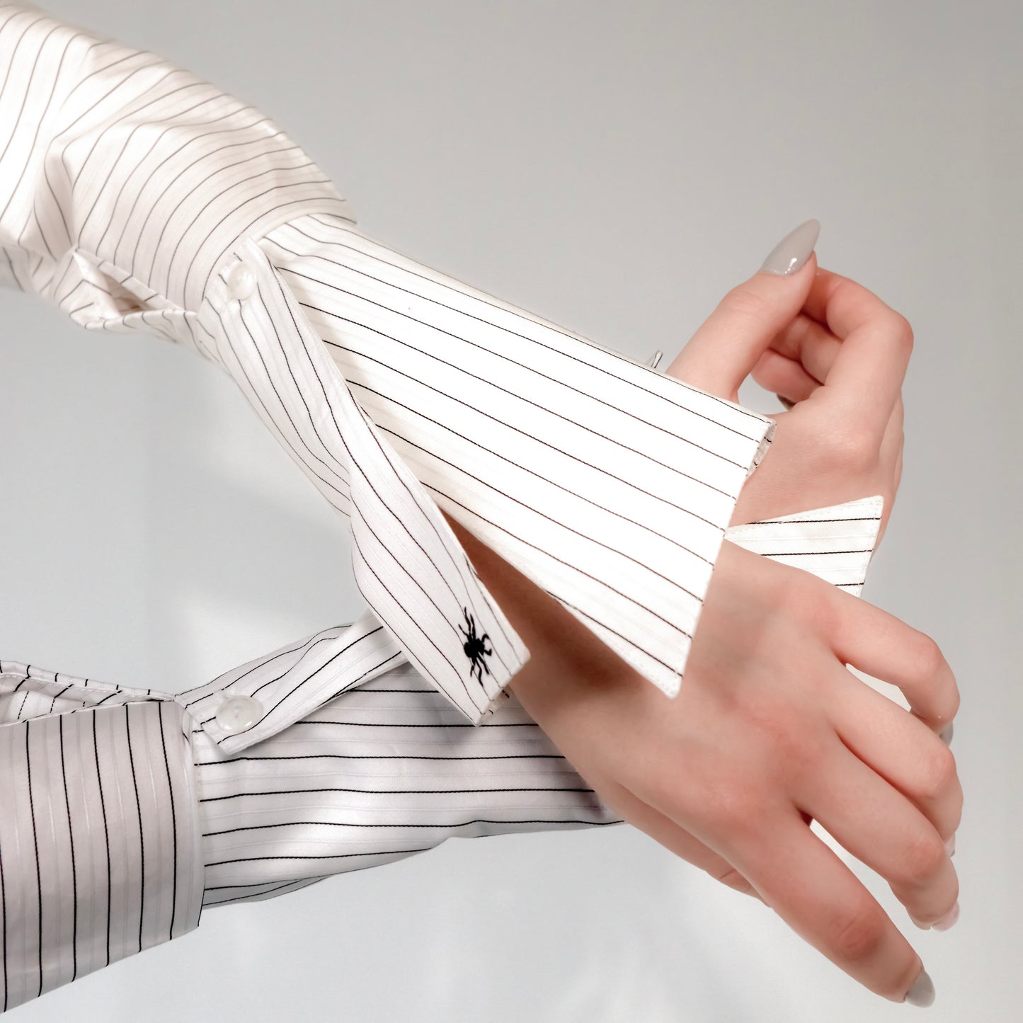 Close-up of a hand wearing a white shirt with black stripes on a light gray background