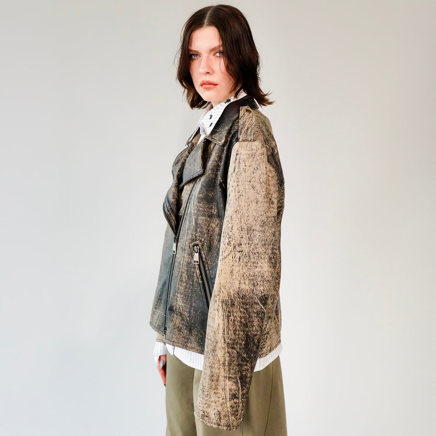 Person wearing a patterned black and brown soft lambskin leather aviator style jacket over a white shirt with black embroidered ant designs on a light gray background. made by mucina studio in latvia