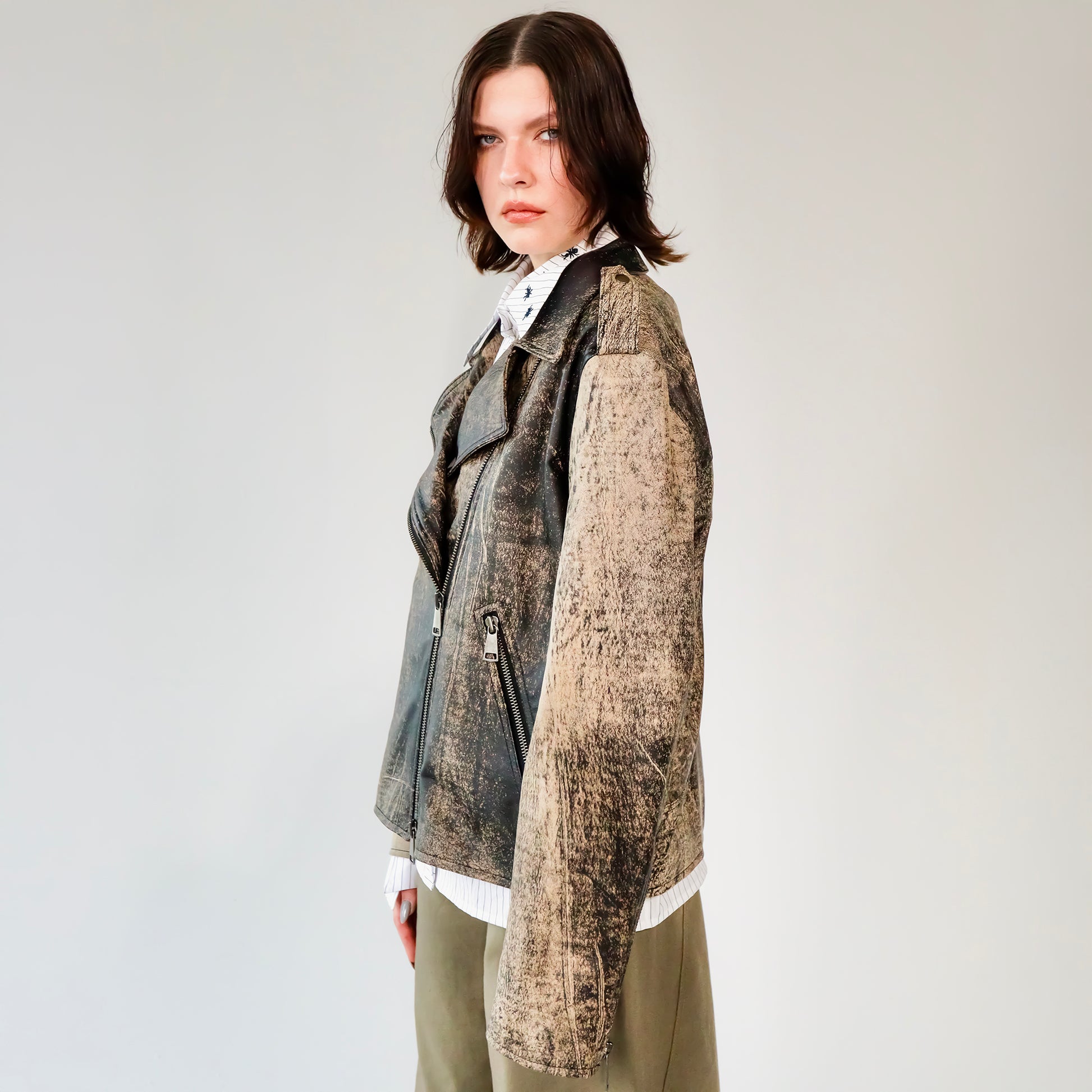 Person wearing a patterned black and brown soft lambskin leather aviator style jacket over a white shirt with black embroidered ant designs on a light gray background. made by mucina studio in latvia