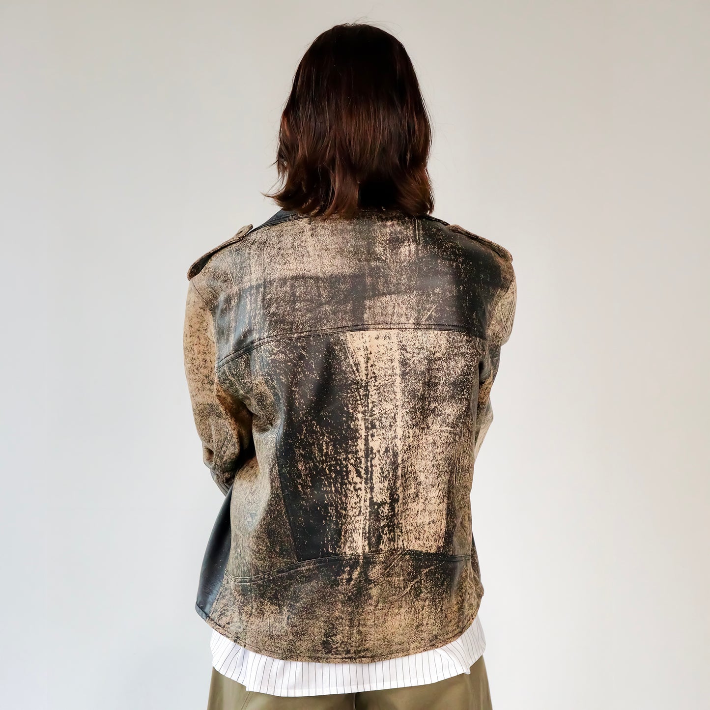 Person wearing a patterned black and brown soft lambskin leather aviator style jacket over a white shirt with black embroidered ant designs on a light gray background. made by mucina studio in latvia