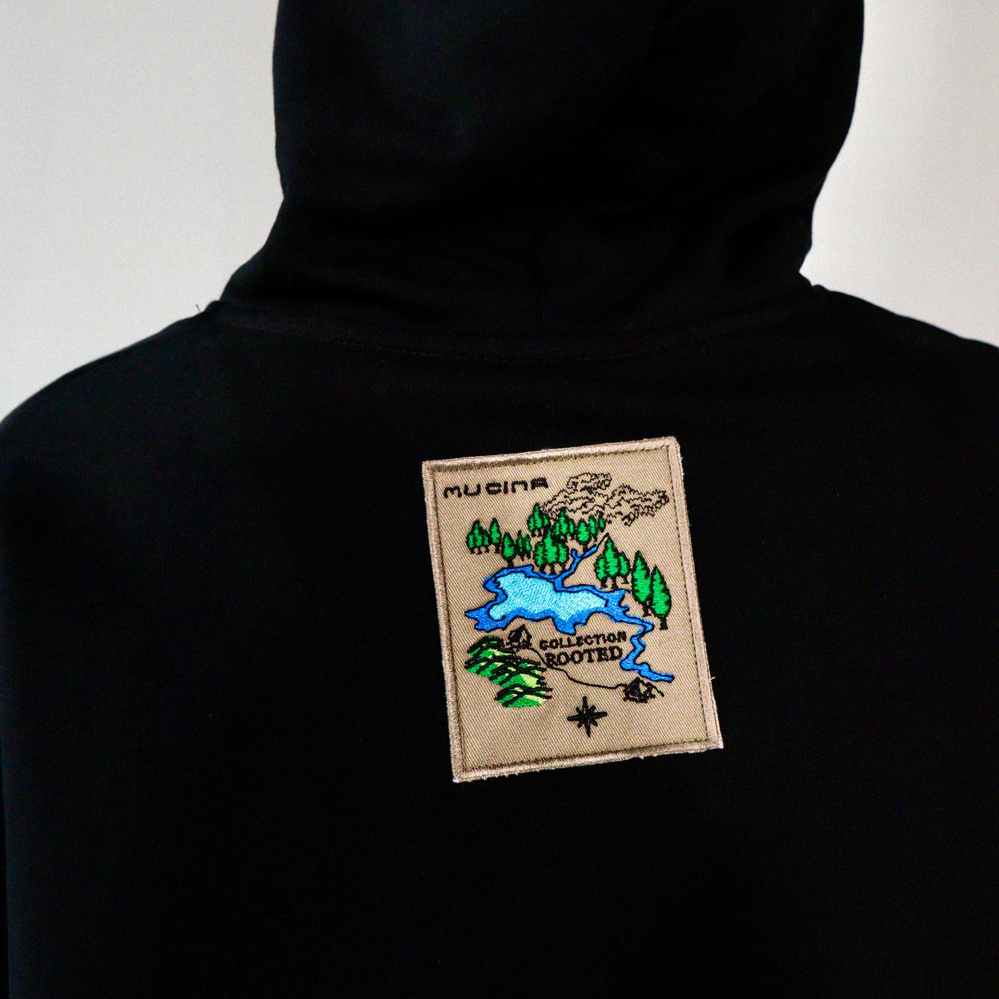 Black hoodie with a embroidered patch on the back against a white background