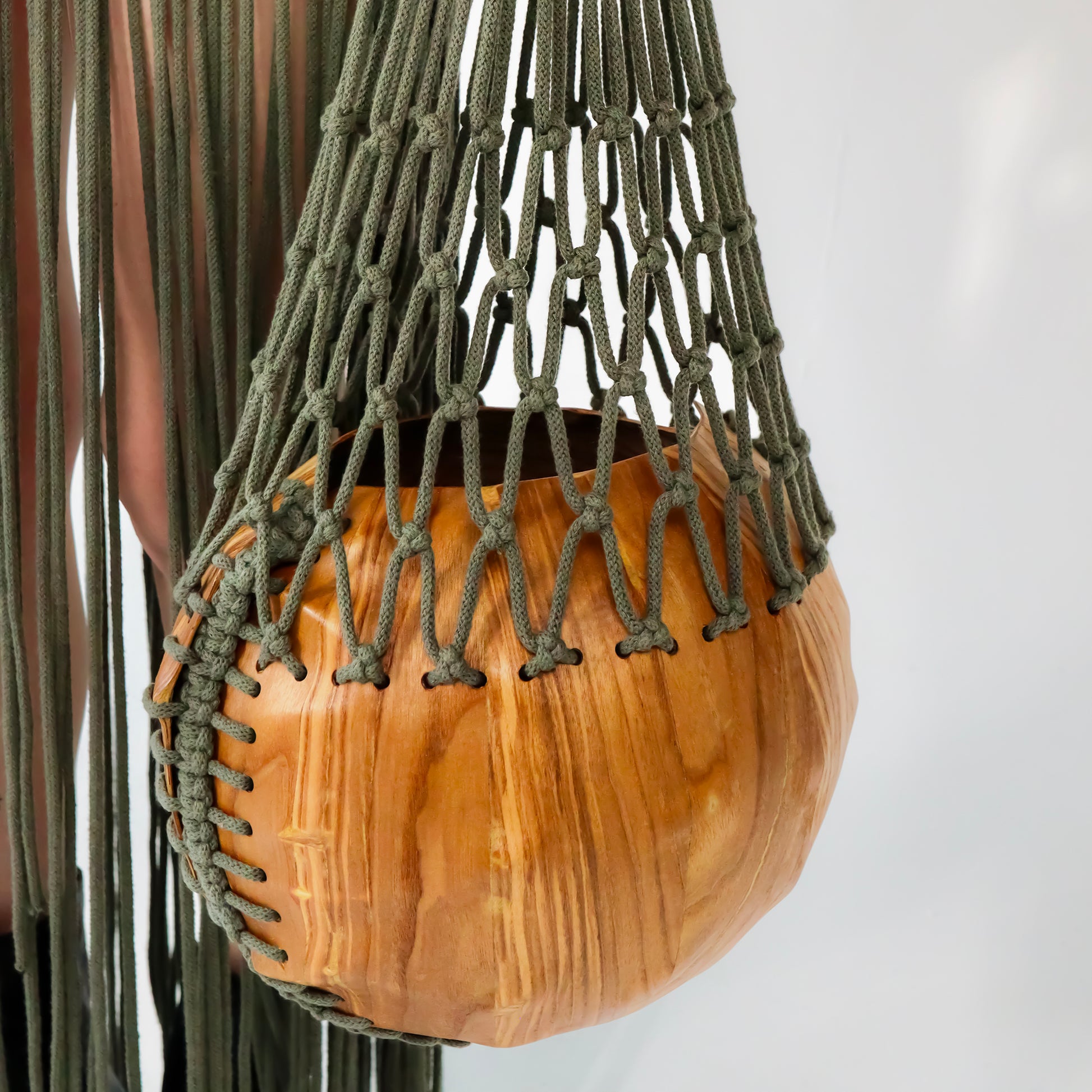 Wooden circular bag with a macrame handle next to a macrame skirt on a white background
