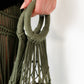 Green macrame bag hanger held by a hand against a white background