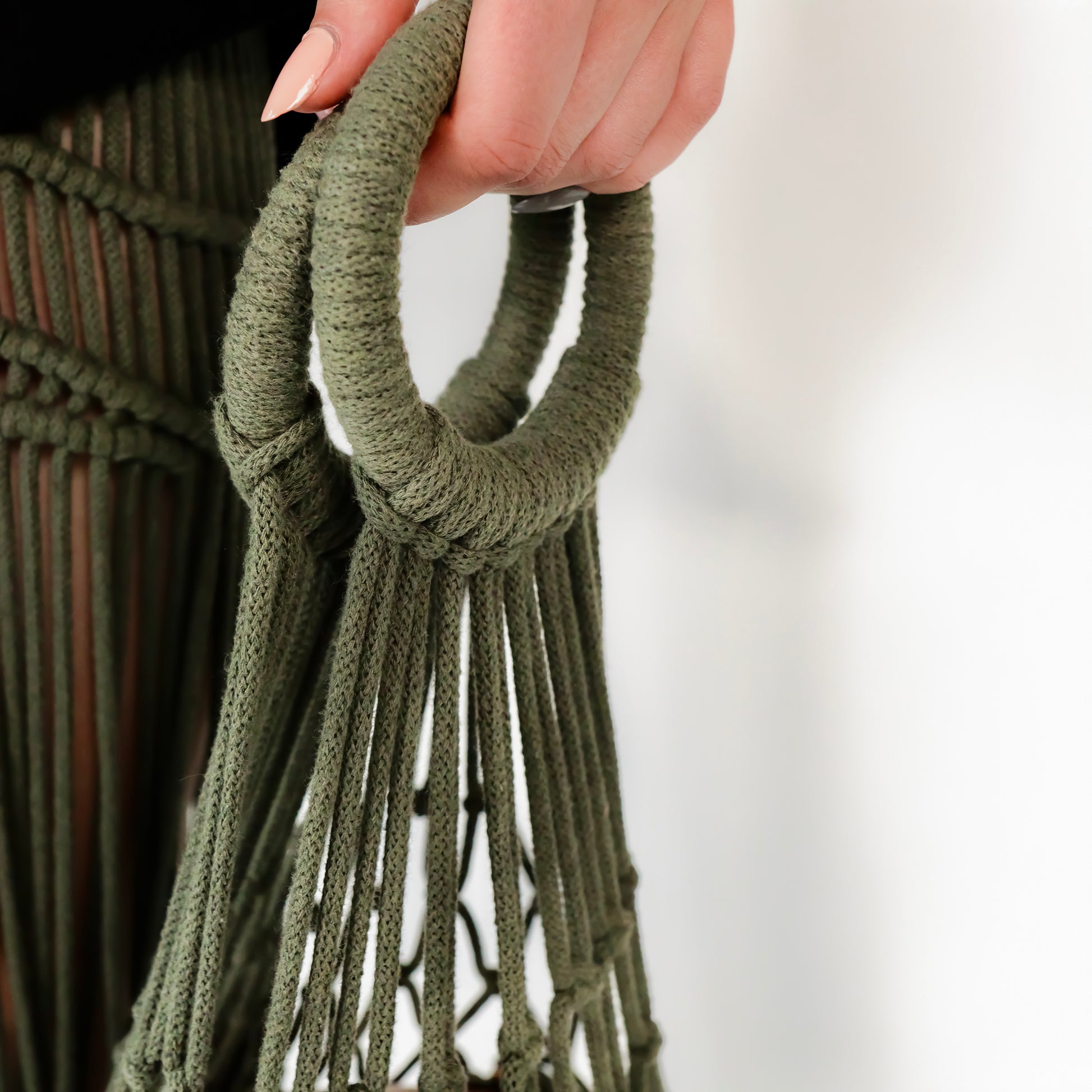 Green macrame bag hanger held by a hand against a white background