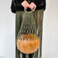 Person holding a green macrame bag with a wooden ball against a white background