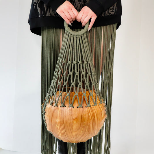 Person holding a green macrame bag with a wooden ball against a white background