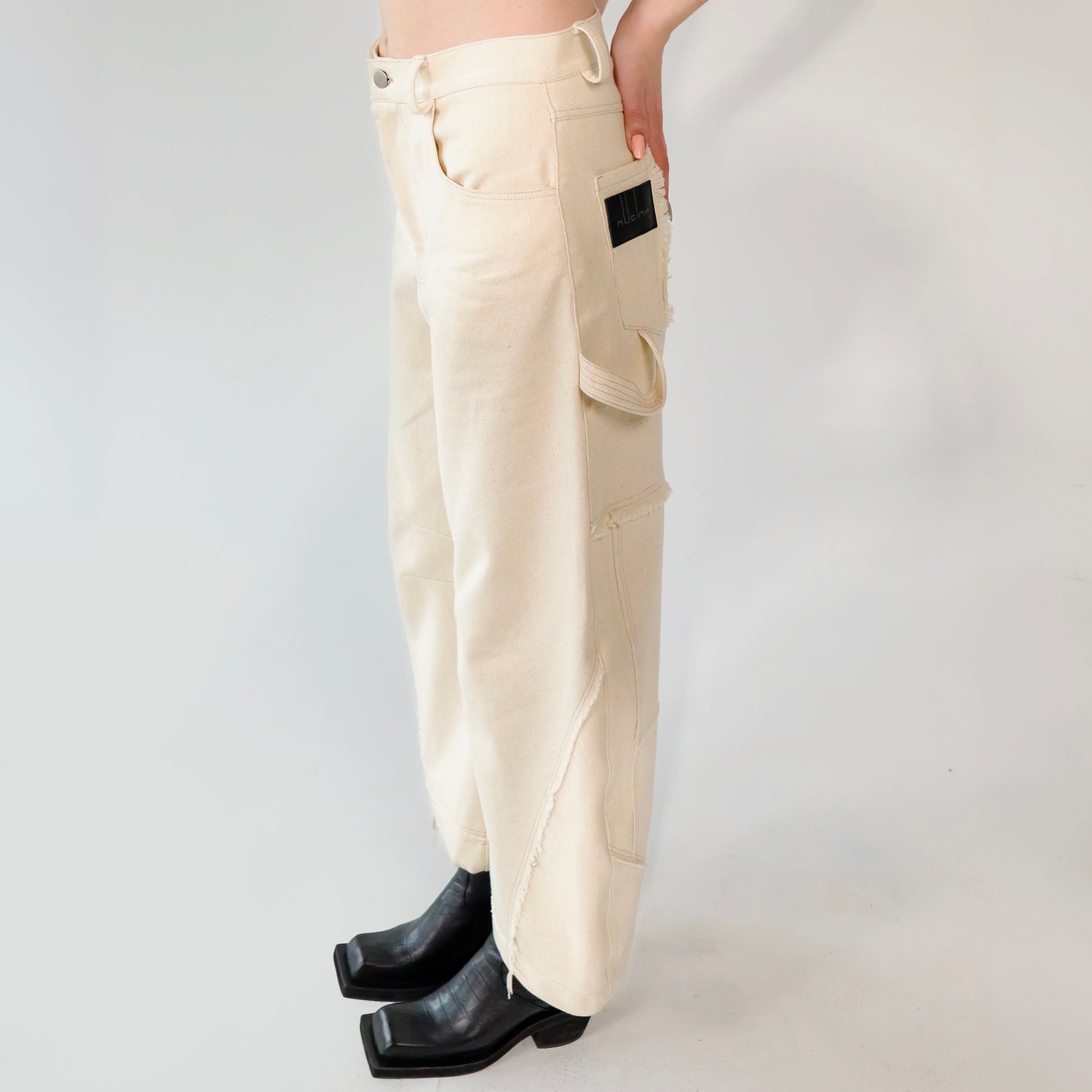Beige barrel-leg cargo pants with patch detailing worn with a beige bomber jacket on a white background