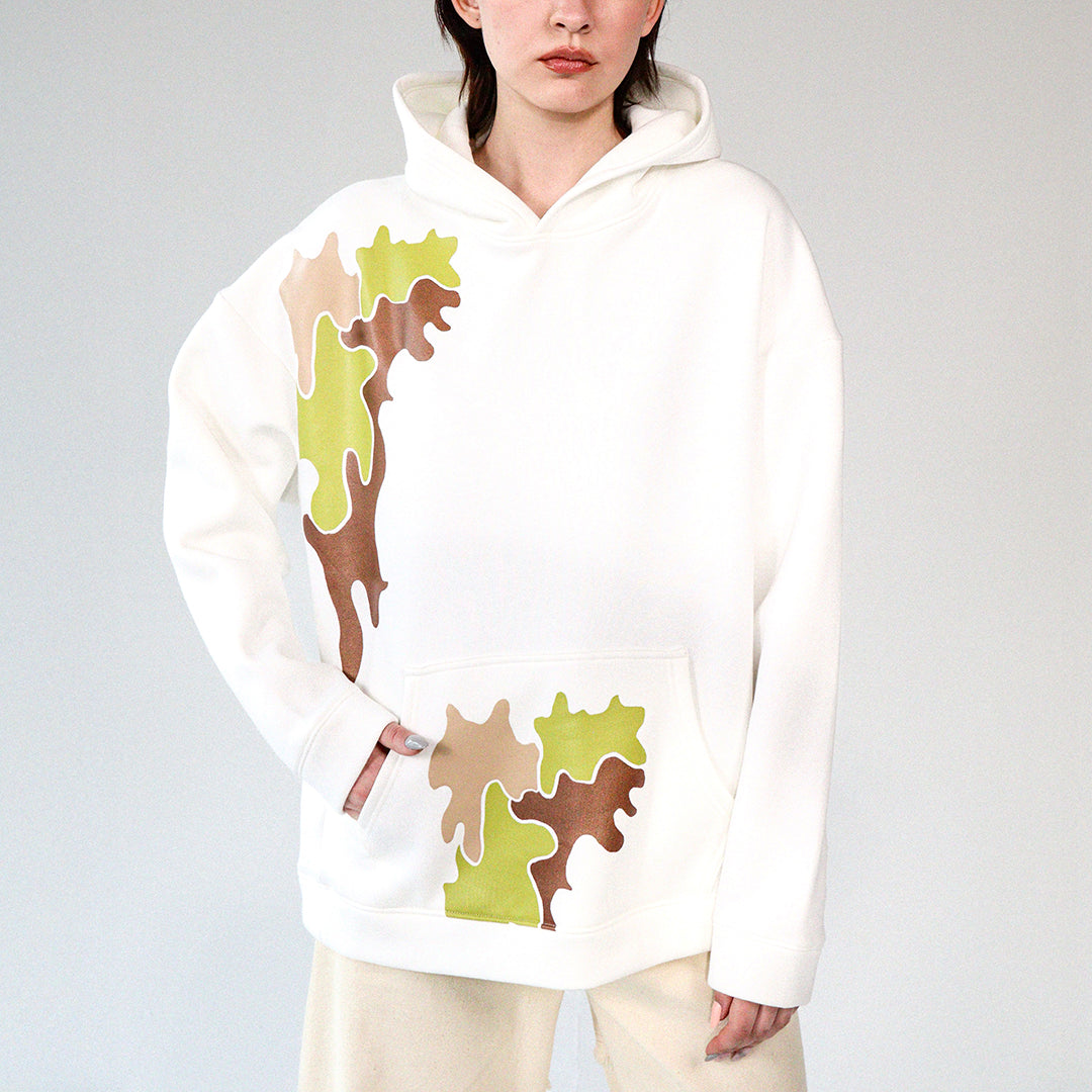 Woman wearing a white hoodie with camouflage brown and green printed pattern  on a gray background