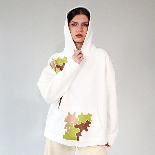 Woman wearing a white hoodie with camouflage brown and green printed pattern on a gray background