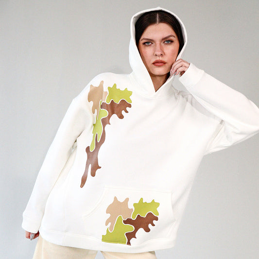 Woman wearing a white hoodie with camouflage brown and green printed pattern on a gray background