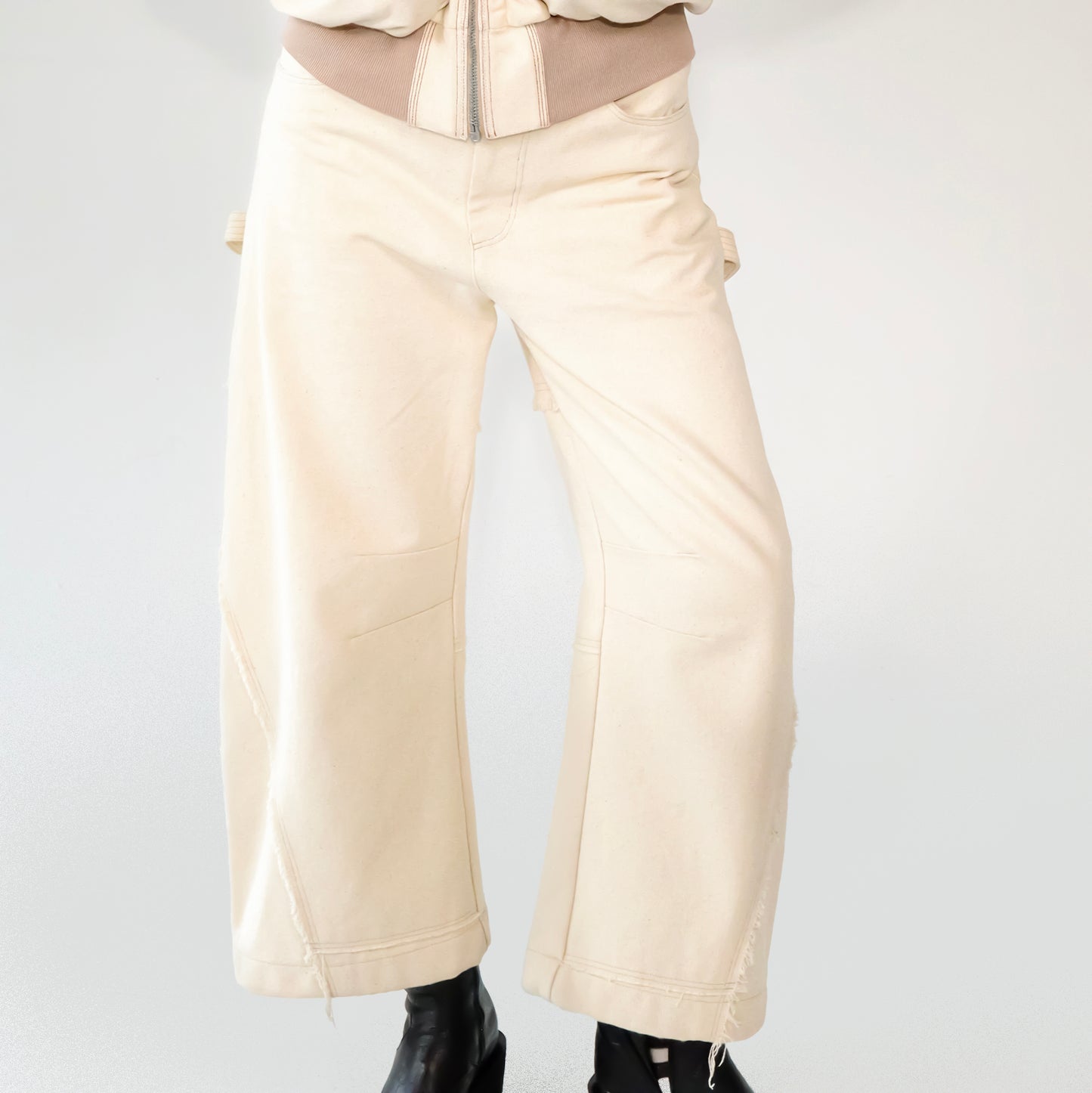 Beige barrel-leg cargo pants with patch detailing worn with a beige bomber jacket on a white background