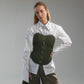 Woman wearing a white shirt with hand embroidered  ant illustrations under a green front lace up corset and khaki wide leg trousers against a gray background