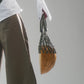 Person holding a half circle wood bag with woven macrame handle next to a person wearing cotton front lace up corset over a button up top and wide leg trousers