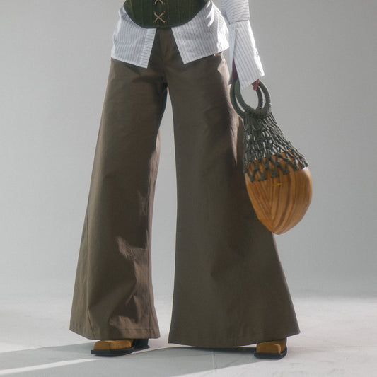 person wearing Khaki wide leg cotton trousers, extra long for tall people holding a wood statement round bag with macrame handle