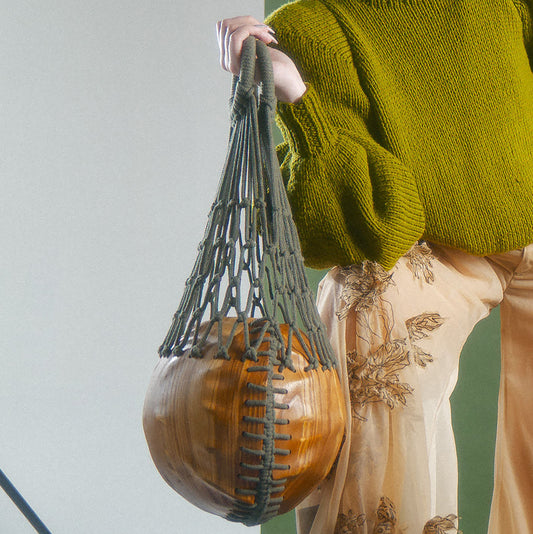 Person holding a circular wood bag with woven macrame handle next to a person wearing hand knit puffed sleeve sweater and machine embroidered sheer wide leg trousers