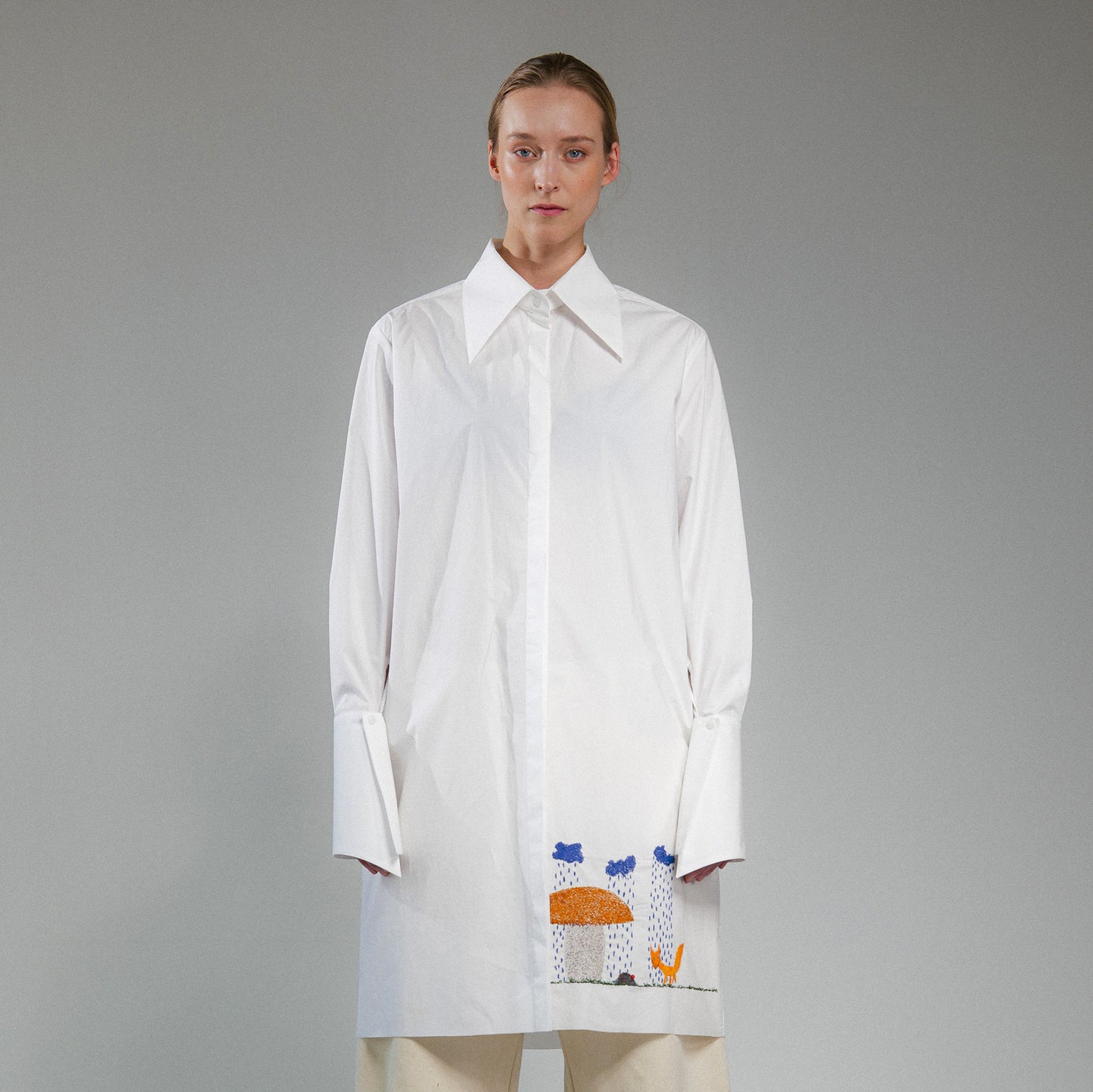 Person wearing a white button up long shirt with hand embroidered designs on a gray background