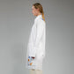 Person wearing a white button up long shirt with hand embroidered designs on a gray background
