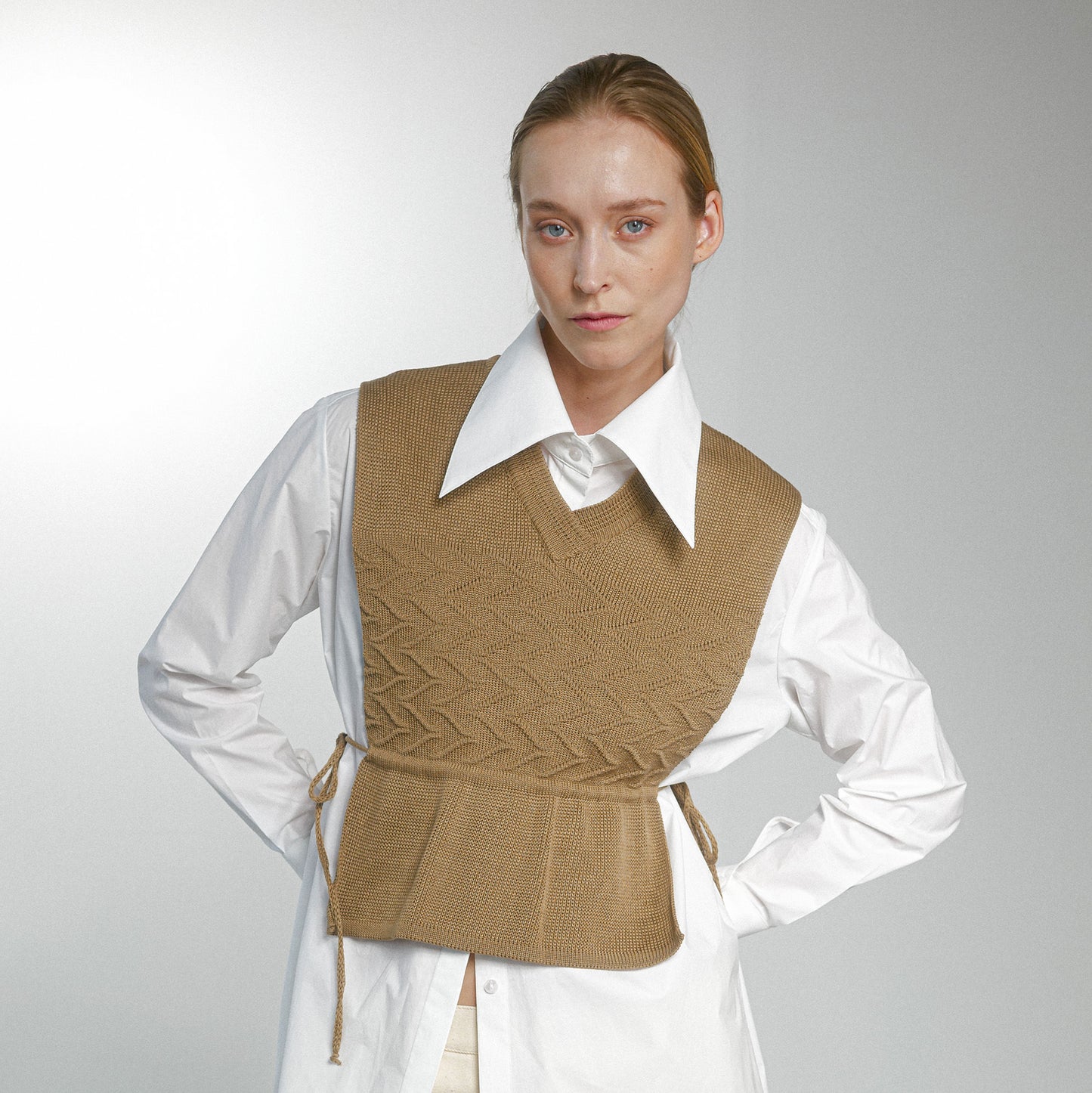 Woman wearing a beige knitted vest over a white shirt on a plain background