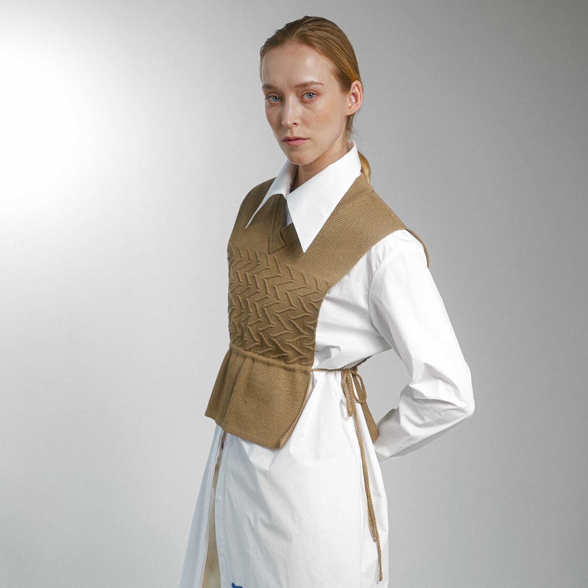 Woman wearing a brown patterned vest over a white shirt on a gray background