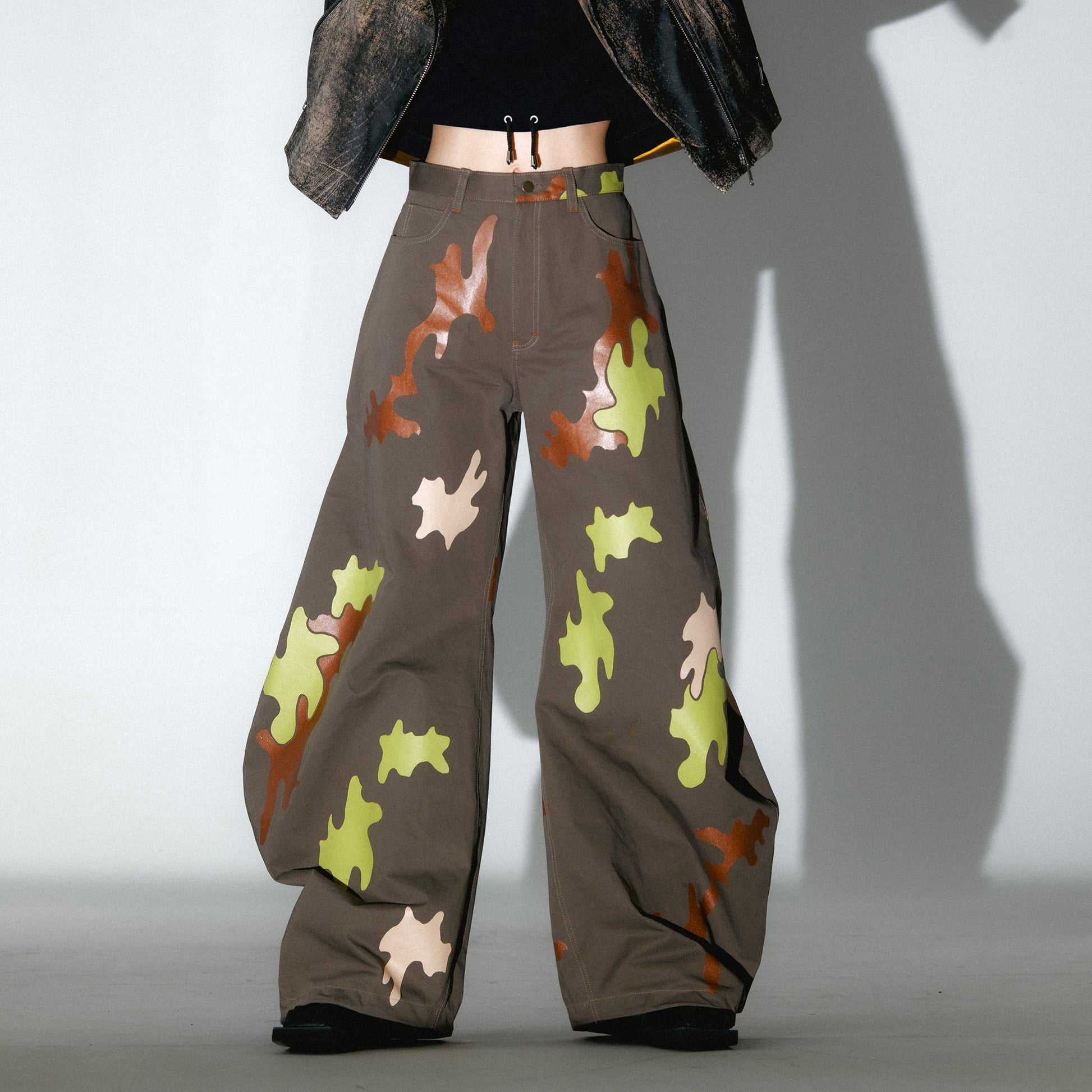Person wearing camouflage-patterned barrel leg pants with a cropped hoodie, photo on white background with intense shadow