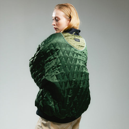 Person wearing reversible green bomber jacket with quilted details on a white background 