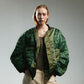 Person wearing reversible green bomber jacket with quilted details on a white background 