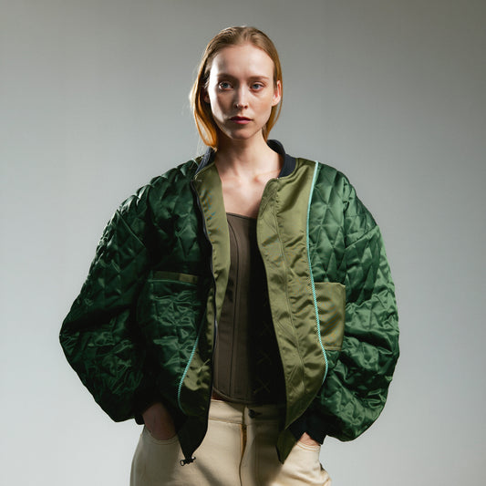 Person wearing reversible green bomber jacket with quilted details on a white background 
